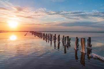 Obraz premium sunset on a pink salt lake, a former mine for the extraction of pink salt. row of wooden pegs overgrown with salt.