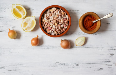 Prebranac ingredients. Balkan baked beans. Serbian, Montenegrin, Bosnian, Croatian, Slovenian cuisine. Uncooked beans, onion, lemon, paprika powder. White wooden background. Top view. Space for text