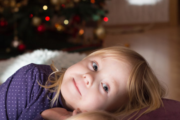 girl smiling and laying on a pillow in front of a christmas tree 