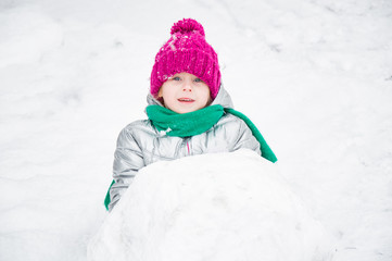 Cute little girl is rolling snowball. children make  snowman in the yard