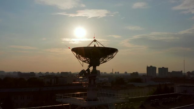 Aerial shot of big satellite antenna for space communications on a roof of building at sunset. Landscape of ex-soviet city at background