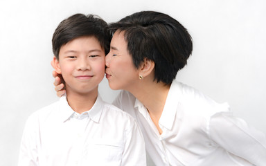 Studio portrait of a beautiful middle aged asian mother gently kiss her preteen son with love and...