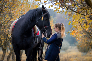 A young, beautiful girl on a walk with a horse in early autumn walks in the park.