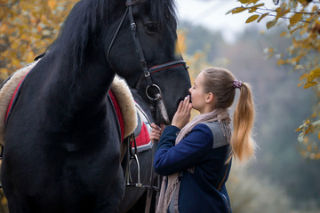 A young, beautiful girl on a walk with a horse in early autumn walks in the park.