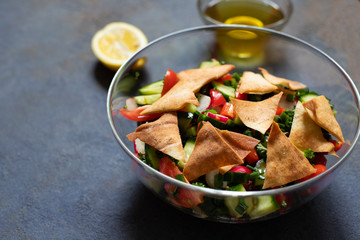 Traditional Fattoush salad  with vegetables and pita bread. Levantine, Arabic, Middle Eastern cuisine. Served in a glass plate with lemon, pita and olive oil. Dark background. Close up