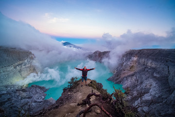 Man traveler standing on edge of crater with colorful sky at morning. Beautiful Ijen volcano with...