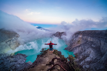 Man traveler standing on edge of crater with colorful sky at morning. Beautiful Ijen volcano with acid lake and sulfur gas going from crater, Indonesia © stryjek
