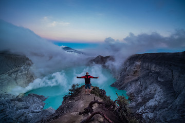 Fototapeta na wymiar Man traveler standing on edge of crater with colorful sky at morning. Beautiful Ijen volcano with acid lake and sulfur gas going from crater, Indonesia