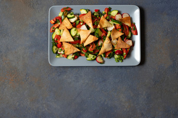 Traditional Fattoush salad  with vegetables and pita bread. Levantine, Arabic, Middle Eastern cuisine. Served in a rectangular plate with lemon and olive oil. Dark background. Top view. Space for text