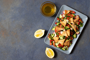 Traditional Fattoush salad  with vegetables and pita bread. Levantine, Arabic, Middle Eastern cuisine. Served in a rectangular plate with lemon and olive oil. Dark background. Top view. Space for text