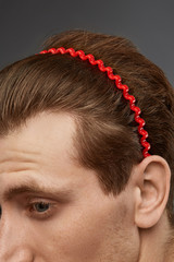 Naklejka premium Extreme close-up shot of a young chestnut European man with a fire red hairband in the form of a wavy wire in his hair. The fashion model with an unshaved cheek-bone is looking away. 