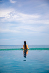 Woman relaxing in infinity swimming pool with sea view, vacation in tropics