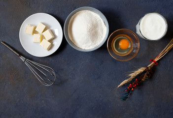 Ingredients for crepes and pancakes on a dark background. Flour, egg, milk, butter, whisk. Top view. Space for text