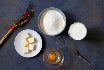 Ingredients for crepes and pancakes on a dark background. Flour, egg, milk, butter, whisk. Top view. Space for text