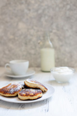 Cottage cheese pancakes, Cheesecakes on the table. Syrniki or sirniki. Healthy breakfast. White dishes. Bottle of milk. A cup of milk. Yogurt or sour cream. White background. Close up