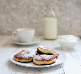Cottage cheese pancakes, Cheesecakes on the table. Syrniki or sirniki. Healthy breakfast. White dishes. Bottle of milk. A cup of milk. Yogurt or sour cream. White background. Close up