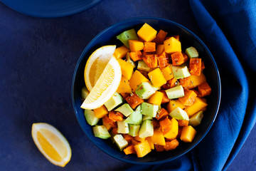 Pegan salad with mango, avocado and sweet potatoes, served with lemon water. Paleo diet. Pegan diet. Vegetarian food. Dark blue background