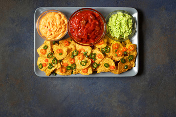 Mexican yellow corn tortilla chips nachos with jalapeno, guacamole, cheese sauce and salsa on dark blue background