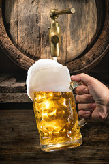 Hand of man is pouring a large lager beer in tap from wooden beer barrel