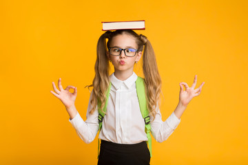 Elementary School Girl Meditating Holding Book On Head, Yellow Background