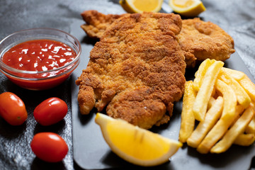 Traditional chicken schnitzel served with french fries, sauce and lemon. Black background. Close-up...