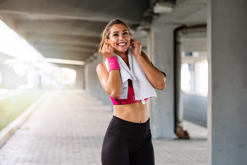 Fototapeta na wymiar Portrait of adorable charming smiling young shape fitness girl with earphones holding a towel and posing. Fitness woman taking a break after running workout.