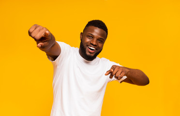 Cheerful african man happily indicating at camera, yellow studio background