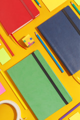 Composition of several stationery notebooks of different colors and stationery on a yellow...