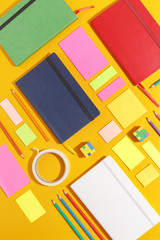 Composition of several stationery notebooks of different colors and stationery on a yellow background. Creative concept of stationery and school supplies. Top view