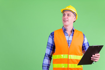 Happy young man construction worker thinking while holding clipboard