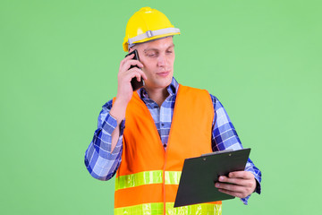 Young man construction worker talking on the phone while holding clipboard