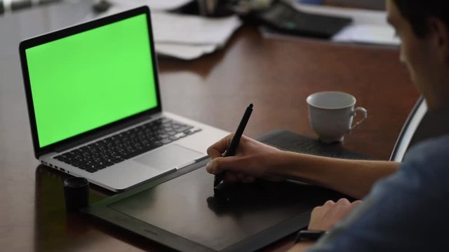 Man drawing on a pen tablet in the office in front of the laptop. Green screen. Close-up shot