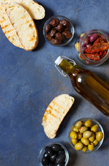 Different types of olives, bruschetta, sun-dried tomatoes and olive oil. Mediterranean snacks. Top view. Dark background. Space for text