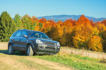 Obraz na płótnie Canvas suv on the gravel country road side in mountains. trees in colorful fall foliage on the background. ridge in the distance. travel by car concept