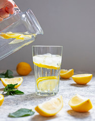 Water with lemon, mint and ice. Water is poured from a glass jug into a glass. Close-up.