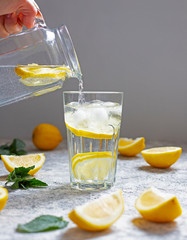 Water with lemon, mint and ice. Water is poured from a glass jug into a glass. Close-up.