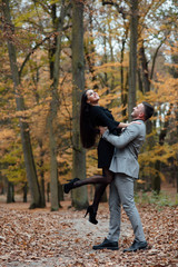 Fototapeta premium Happy young couple in love. The guy holding his girlfriend in his arms. Romantic relationship in autumn forest. Love story. To love each other.