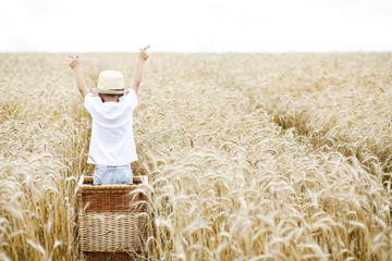 Naklejka na ściany i meble Happy child in summer wheat field. Beautiful boy with in a straw hat with ripe wheat in hands.
