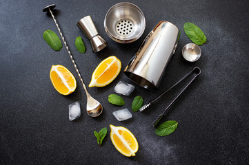 Cocktail shaker and bar tools. Ingredients for a cold alcoholic cocktail. Mojito cocktail. Lemon, mint, ice, rum. Top view, horizontal, black background, copy space