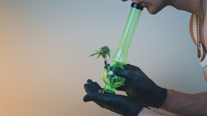 The person hold in his hand bong with fresh medical marijuana buds. Concept of smoking cannabis.