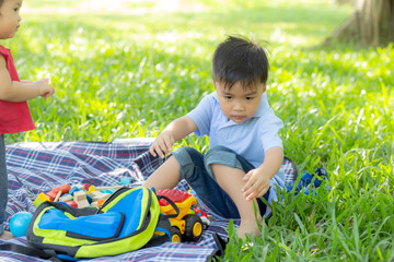 Little boy is playing for idea and inspiration with toy block in the grass field, kid learning with construction block for education, child activity and game in the park with happy in the summer.