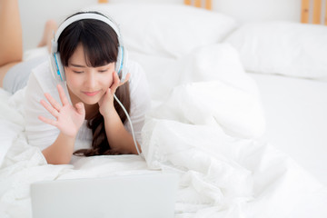 Beautiful young asia woman lying in bedroom using laptop computer showing video call chat at home, girl greet and listen and talking messenger, communication and lifestyle concept.