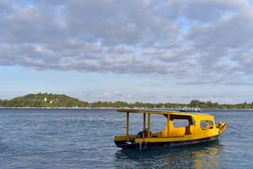 Fototapeta premium Yellow divers boat docked on the shore of Gili Meno Island and Gili Trawangan Island at the background, Indonesia