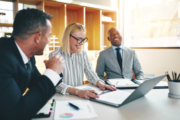 Three laughing businesspeople discussing paperwork together in a