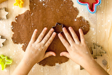 Faceless child preparing Christmas cookies From above crop kid cutting out fir tree shape from dough while cooking ginger biscuits at home