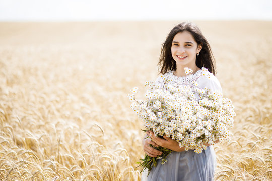 Pretty teen girl standing in a field among wheat. Girl holding a large bouquet of flowers in her hands