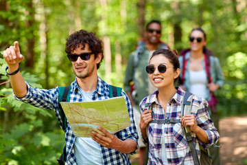 travel, tourism, hike and people concept - group of friends with map and backpacks in forest