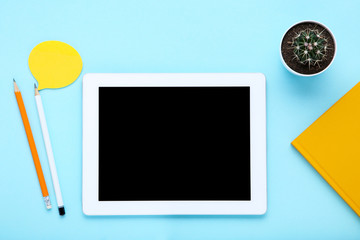 Tablet computer with pencils and cactus on blue background