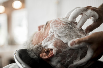 Washing hair of senior male in barbershop