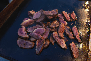 Roasted duck on a grill outdoor. Slices of appetizing fresh meat during frying. Evening meal.